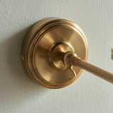Close-up of the Endon Cliffwood Ivy wall light's brushed aged brass backplate and adjustable knuckle joint mounted on a pale textured wall.