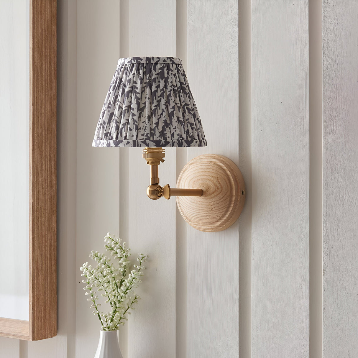 Endon Danemere wall light with natural Ash wood back, brushed brass adjustable arm and pleated grey leaf-print shade, mounted on panelled wall.