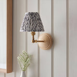 Endon Danemere wall light with natural Ash wood back, brushed brass adjustable arm and pleated grey leaf-print shade, mounted on panelled wall.