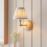 Danemere Wall Light with pleated blue and cream leaf-pattern shade, brass arm and natural Ash wood backplate, shown lit against a panelled wall.