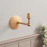 Danemere wall light with round natural ash wood back plate, adjustable brushed brass arm and B22 bulb holder, shown mounted on a light grey wall.