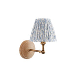 Danemere wall light with natural Ash wood backplate, brushed brass adjustable arm and pleated blue leaf-print fabric shade, shown on a white background.