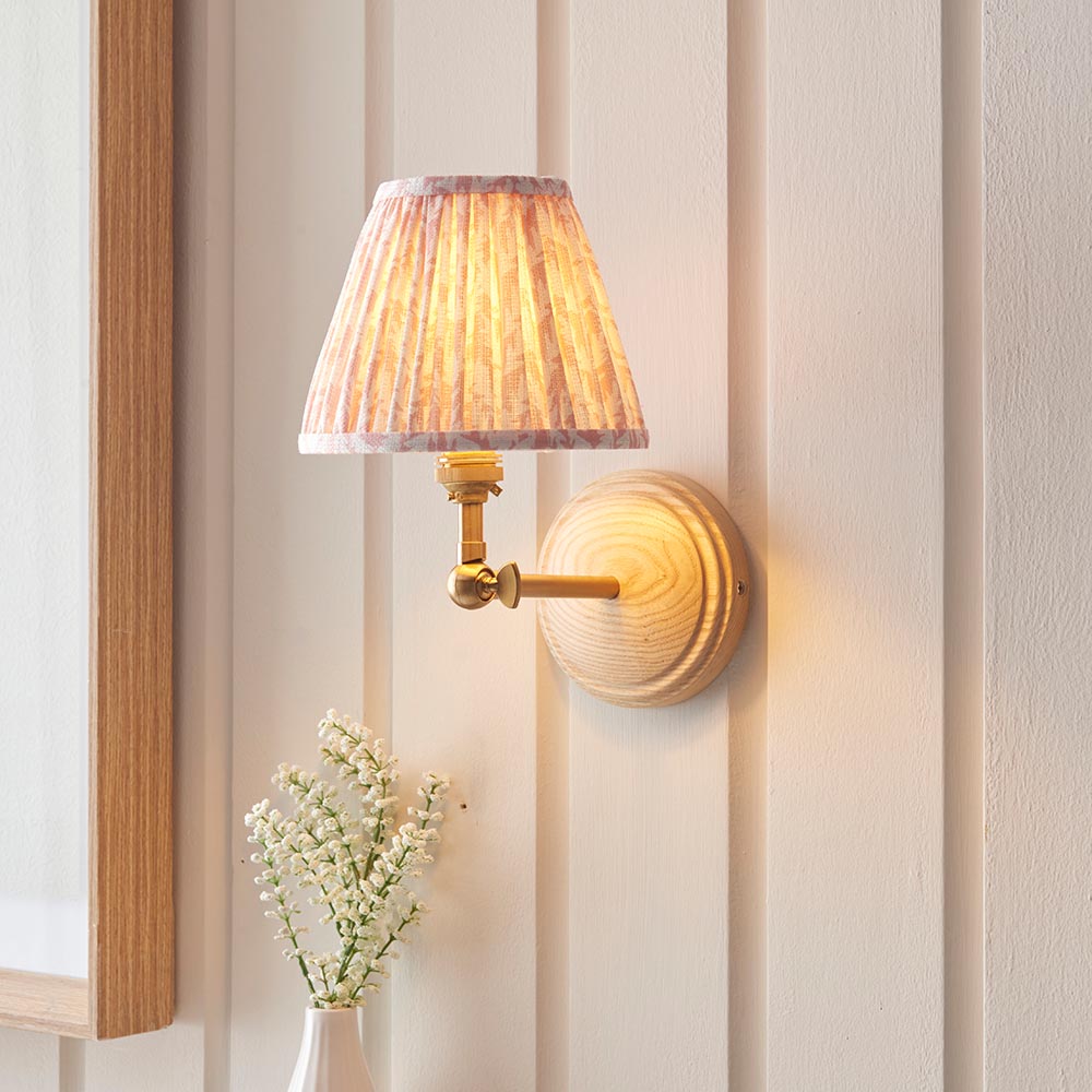 Endon Danemere wall light with Ash wood back, brushed brass adjustable arm and pleated peach Leaf-print faux linen shade, mounted on panelled wall.