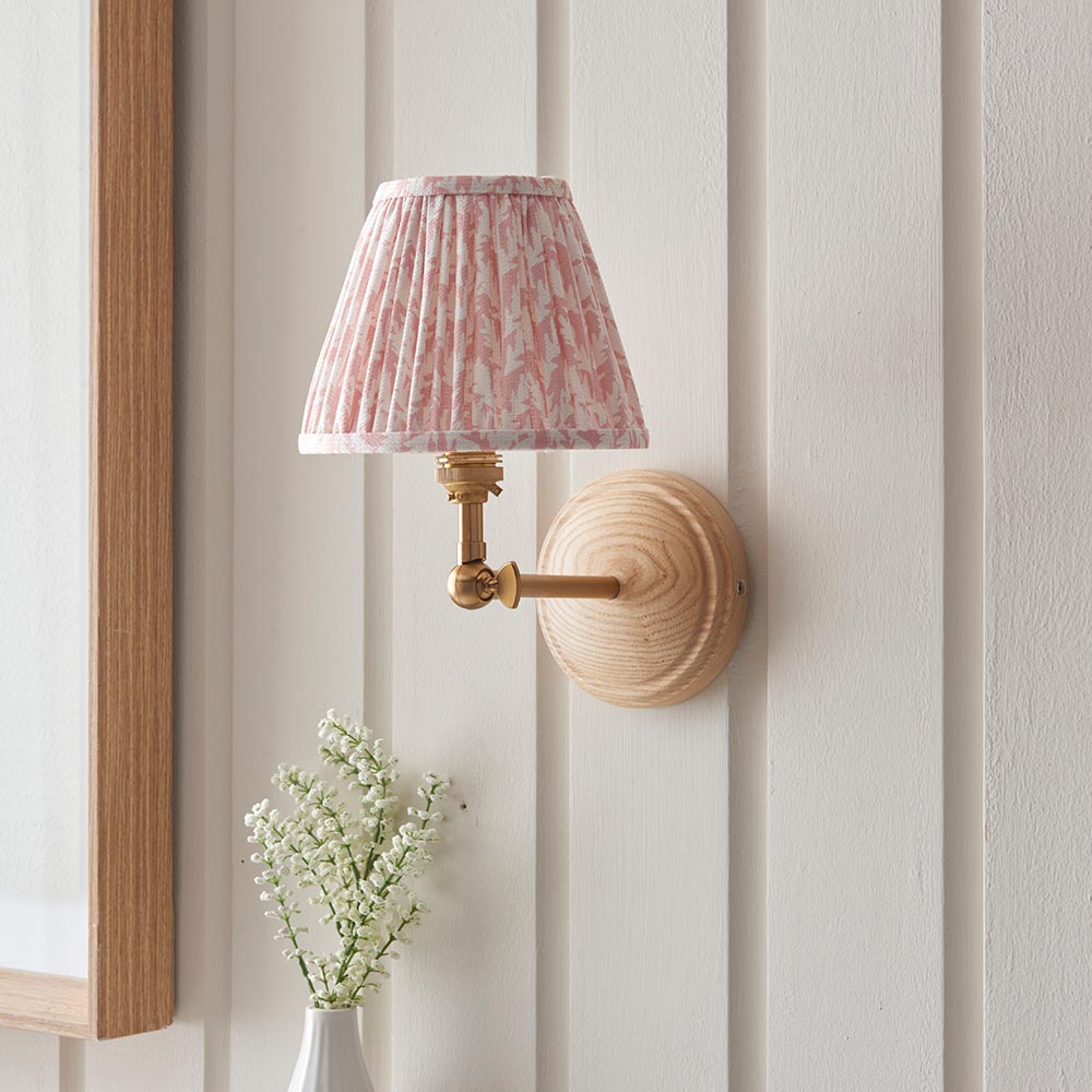 Endon Danemere wall light with natural Ash wood back, brushed aged brass adjustable arm and pleated peachy Leaf faux linen shade on panelled wall.
