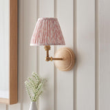 Endon Danemere wall light with natural Ash wood back, brushed aged brass adjustable arm and pleated peachy Leaf faux linen shade on panelled wall.