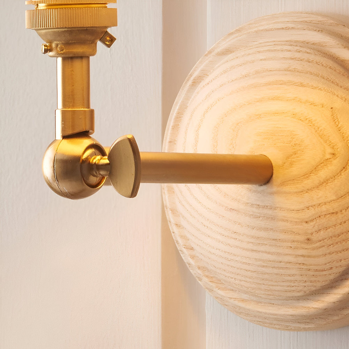 Danemere Ripple Wall Light close-up showing brushed brass fitting with ball-joint knuckle and linear arm against a round ash wood back plate.