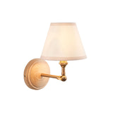 Danemere Ivy wall light featuring an ash wood backplate, brass arm with knuckle joint, and a tapered beige fabric shade, on a white background.