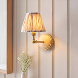 Endon Danemere wall light with natural ash wood back plate, brushed aged brass arm and pleated Ikat faux silk shade, mounted on cream panelling.