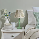 Endon Aldworth Leaf table lamp with green turned spindle base and pleated leaf-print shade on a white bedside table styled with jug, bowls and mug.