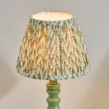 Endon Aldworth Leaf table lamp with pleated green leaf-print fabric shade on a turned green spindle base, shown lit against a neutral background.