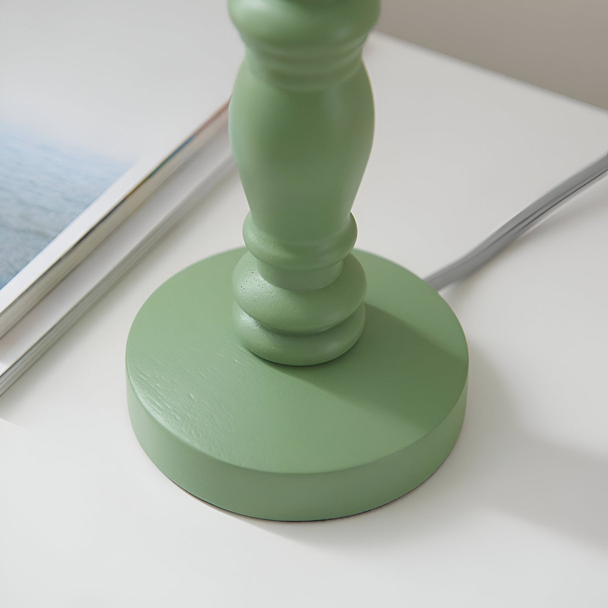 Close-up of the green turned wooden spindle base of the Endon Aldworth Leaf table lamp on a white surface beside an open magazine.
