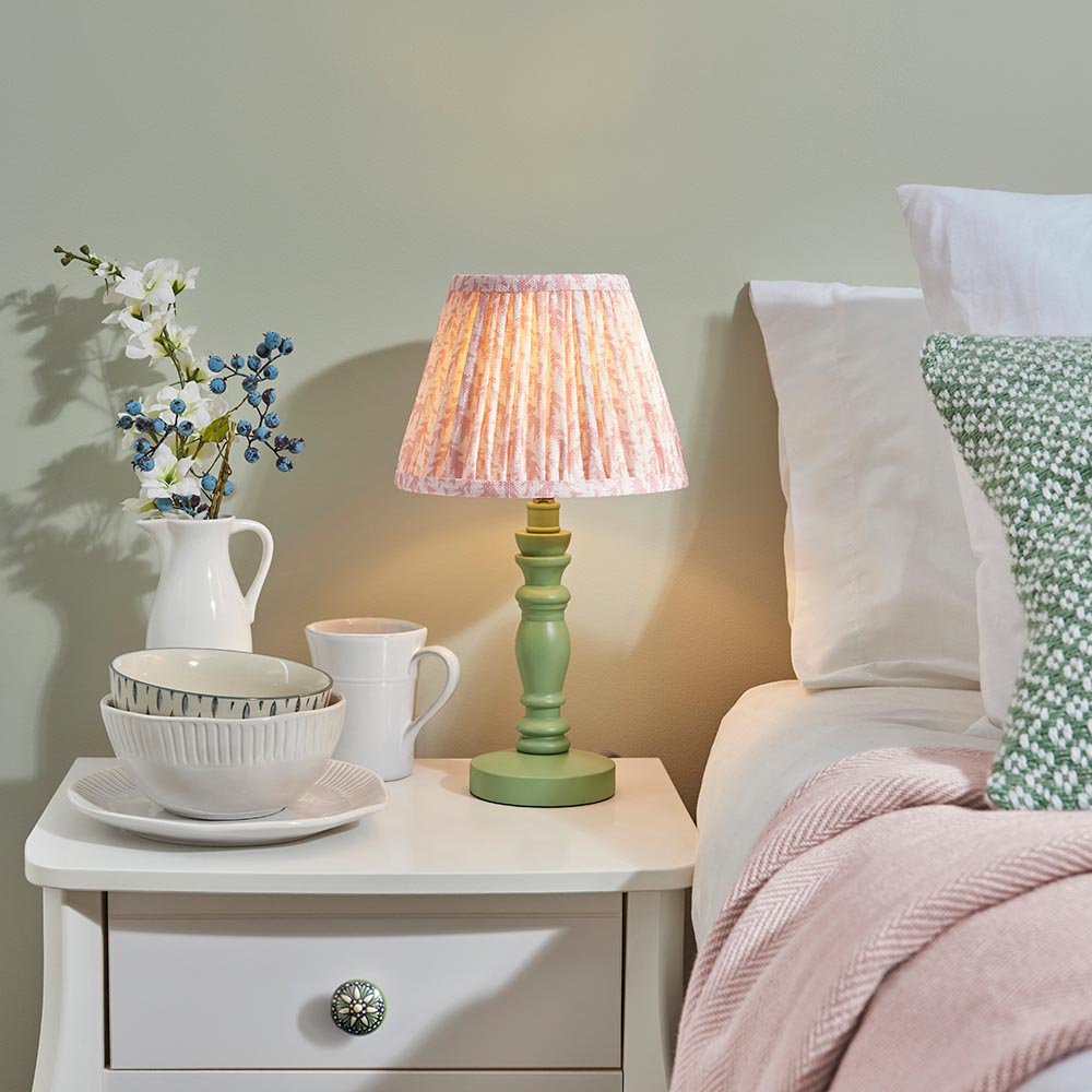 Endon Aldworth Leaf table lamp with green turned spindle base, brass B22 lampholder and pink leaf-print pleated shade, on a bedside table.