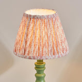 Endon Aldworth Leaf table lamp lit, showing a pleated pink leaf-print fabric shade on a turned green satin-painted wooden spindle base.