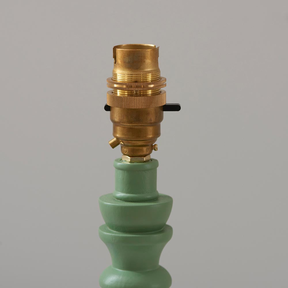 Close-up of the Endon Aldworth Leaf table lamp's brass B22 switched lampholder atop a green turned wooden spindle, on a light grey background.