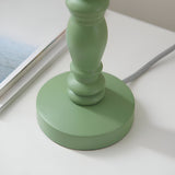 Close-up of the green satin painted turned wooden base of the Endon Aldworth Ripple table lamp with grey braided flex, beside a magazine.