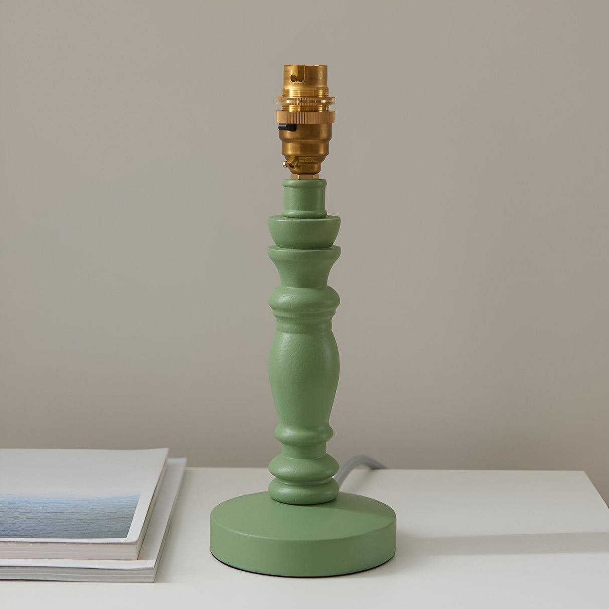 Endon Aldworth table lamp base in green with turned wooden spindle and brass B22 lamp holder, shown on a light surface beside a book.