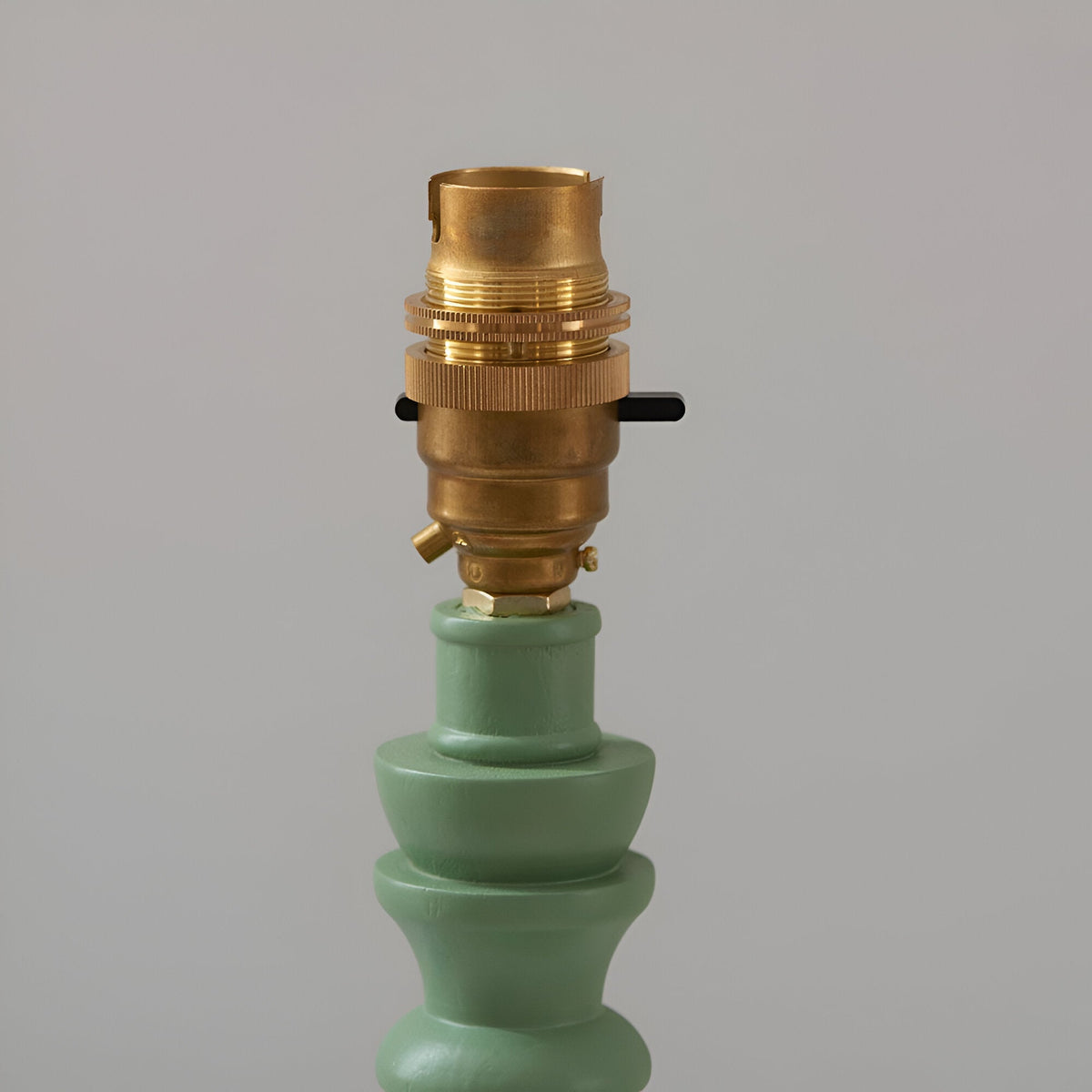 Close-up of the brass B22 switched lamp holder on the green turned wooden spindle base of the Endon Aldworth Zigzag Table Lamp on light grey.