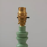 Close-up of the brass B22 switched lamp holder on the green turned wooden spindle base of the Endon Aldworth Zigzag Table Lamp on light grey.