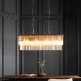 Bevstead 4-light linear pendant with brushed brass band and clear glass drops, hung from twin chains over a dining table in a dark-panelled room.