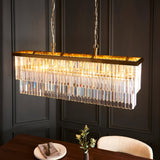 Bevstead 4 Light Linear Pendant in brushed brass with crystal glass drops, hung on twin chains above a dining table in a dark panelled room.
