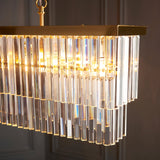 Bevstead 4 Light Linear Pendant in brushed brass with faceted glass drops on a straight metal bar, shown against a dark panelled wall.