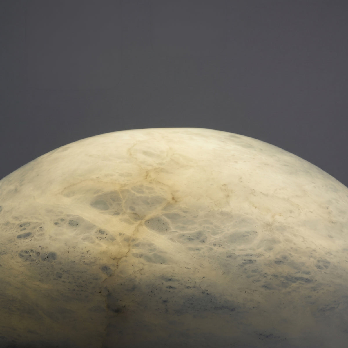 Close-up of the Morfia Small Mushroom Alabaster Table Lamp's domed top, showing natural stone veining glowing softly against a plain grey background.