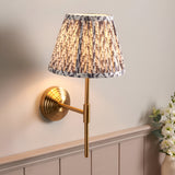 Castleigh Leaf Wall Light in Grey, brass-finish stepped backplate and T-shaped arm with a pleated leaf-print tapered shade, shown lit on a light wall.