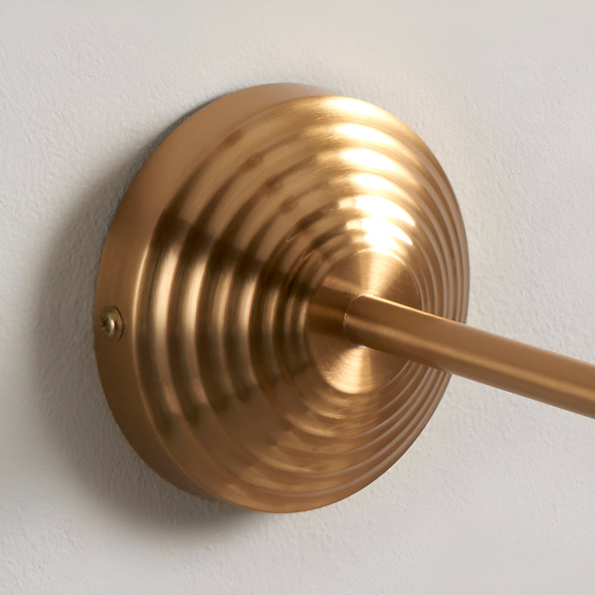 Close-up of the Castleigh Leaf Wall Light's stepped, ribbed brushed brass back plate and T-shaped arm against a plain light wall.