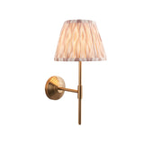 Endon Castleigh Ikat wall light with brushed aged brass stepped backplate, T-shaped arm and tapered pleated cream Ikat fabric shade, on a white background.