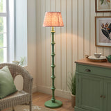 Endon Bevbury Ripple floor lamp with green turned wood spindle base and pink pleated faux linen shade, styled beside a wicker chair and green sideboard.