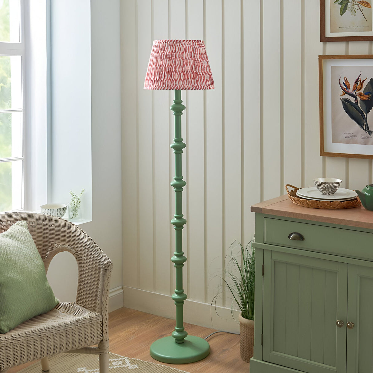 Endon Bevbury Ripple floor lamp with green turned wood spindle base and pink patterned pleated shade, set beside a wicker chair and sage green sideboard.