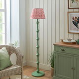 Endon Bevbury Ripple floor lamp with green turned wood spindle base and pink patterned pleated shade, set beside a wicker chair and sage green sideboard.