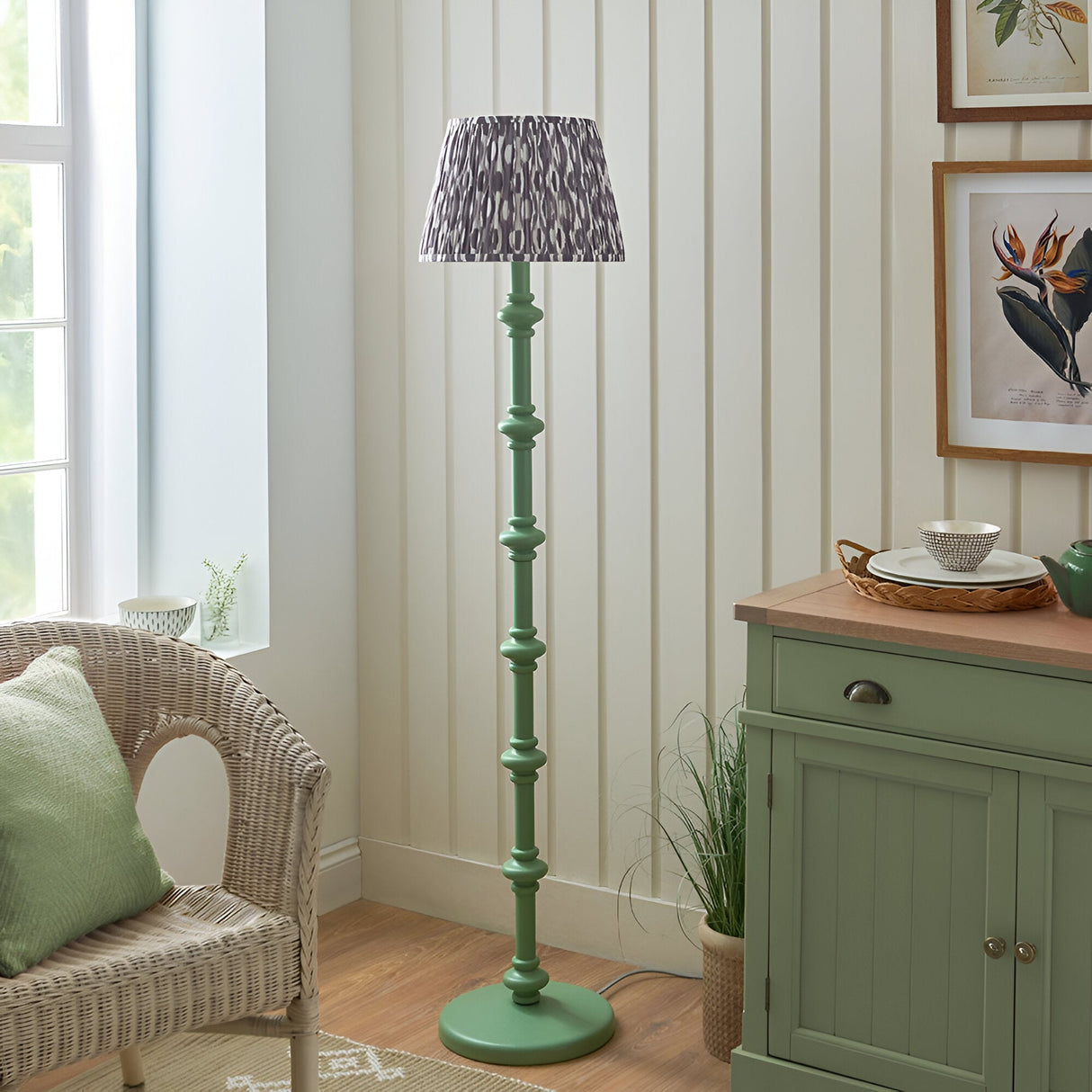 Endon Bevbury Ikat floor lamp with green turned wood spindle base and grey patterned pleated shade, styled in a living room beside a wicker chair.
