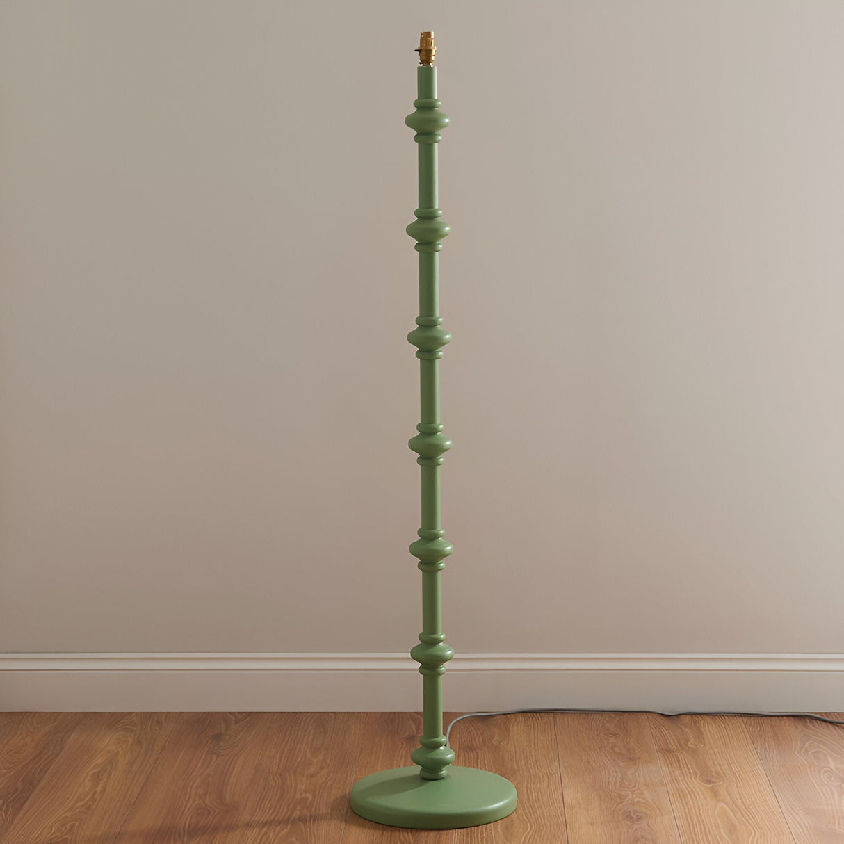 Endon Bevbury floor lamp base in Cotswold green with turned wooden spindle stem and brass B22 lamp holder, shown against a neutral wall on wood flooring.
