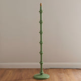 Endon Bevbury floor lamp base in Cotswold green with turned wooden spindle stem and brass B22 lamp holder, shown against a neutral wall on wood flooring.