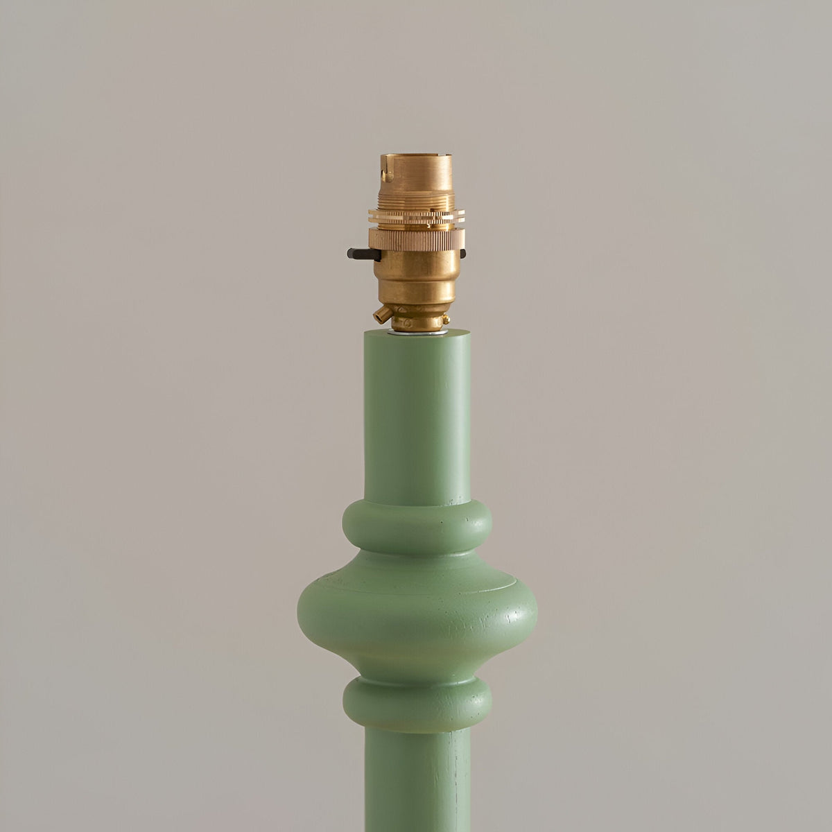 Close-up of the Endon Bevbury floor lamp's green turned wood spindle base with brass B22 switched lamp holder against a neutral background.