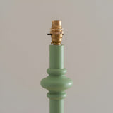 Close-up of the Endon Bevbury floor lamp's green turned wood spindle base with brass B22 switched lamp holder against a neutral background.