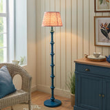 Endon Bevbury Ripple floor lamp with a blue turned wood spindle base and pink patterned pleated shade, beside a wicker armchair and blue sideboard.
