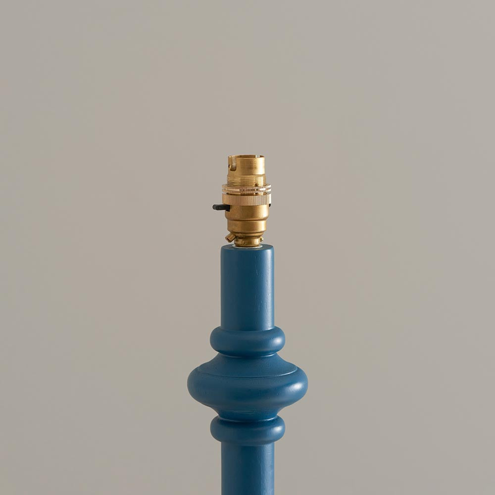 Close-up of Endon Bevbury Ripple floor lamp's blue turned wood spindle base with decorative bulge and switched brass B22 lamp holder on a light background.