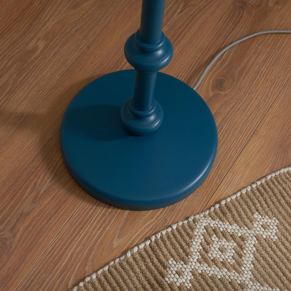 Close-up of the Endon Bevbury Ripple floor lamp's marlin blue turned wood spindle base on wood flooring, beside a woven rug and grey braided flex.