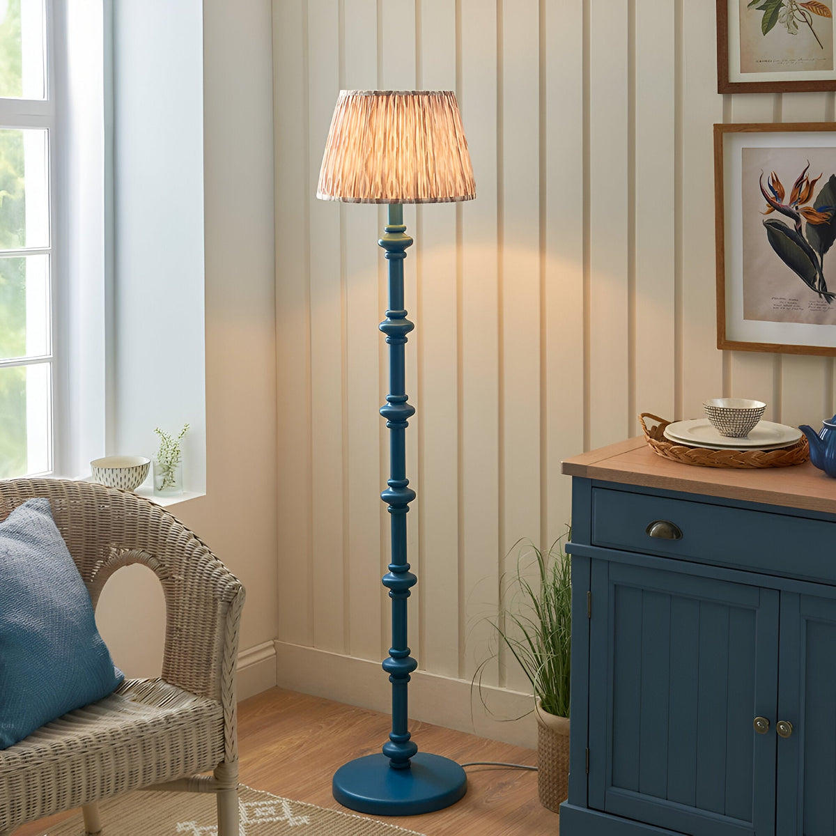 Endon Bevbury Ikat floor lamp with blue turned wood spindle base and pleated patterned shade, styled beside a wicker chair and blue sideboard.