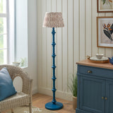 Endon Bevbury floor lamp with blue turned wood spindle base and pleated Ikat faux silk shade, styled beside a wicker chair and blue sideboard.