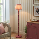 Endon Bevbury Ripple floor lamp with pink turned wood spindle base and pleated ripple shade, beside a wicker chair and pink sideboard in a living room.