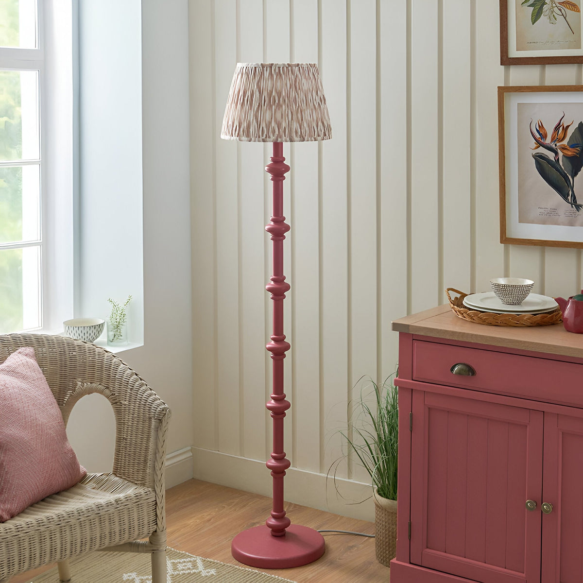 Endon Bevbury floor lamp with pink turned wood spindle base and pleated Ikat fabric shade, styled in a living room beside a wicker chair and pink sideboard.