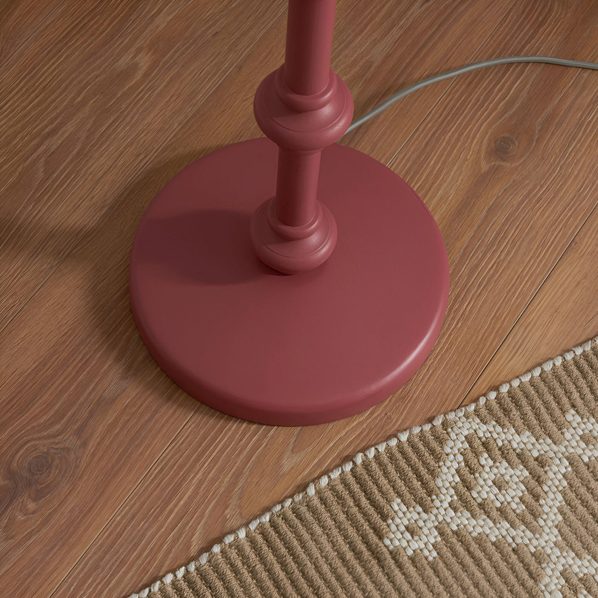 Close-up of the pink clay turned wood spindle base of the Endon Bevbury Ikat floor lamp on wood flooring beside a woven natural rug.