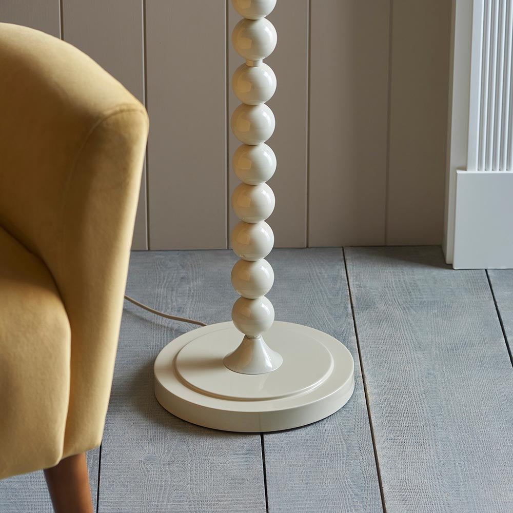 Endon Brenleigh Ripple floor lamp base with glossy white stacked spheres on a round base, beside a yellow armchair on grey plank flooring.