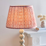 Endon Brenleigh Ripple floor lamp with a pleated white and pink wavy patterned shade on a glossy cream stacked sphere base beside a white mantel.
