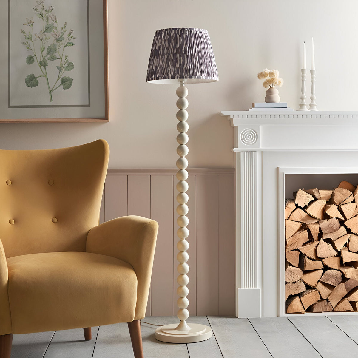 Endon Brenleigh floor lamp with white stacked sphere base and grey Ikat pleated fabric shade, beside a mustard armchair and white fireplace with logs.
