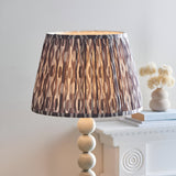 Endon Brenleigh floor lamp with glossy white stacked sphere base and grey Ikat patterned pleated fabric shade, shown lit on a white mantel.