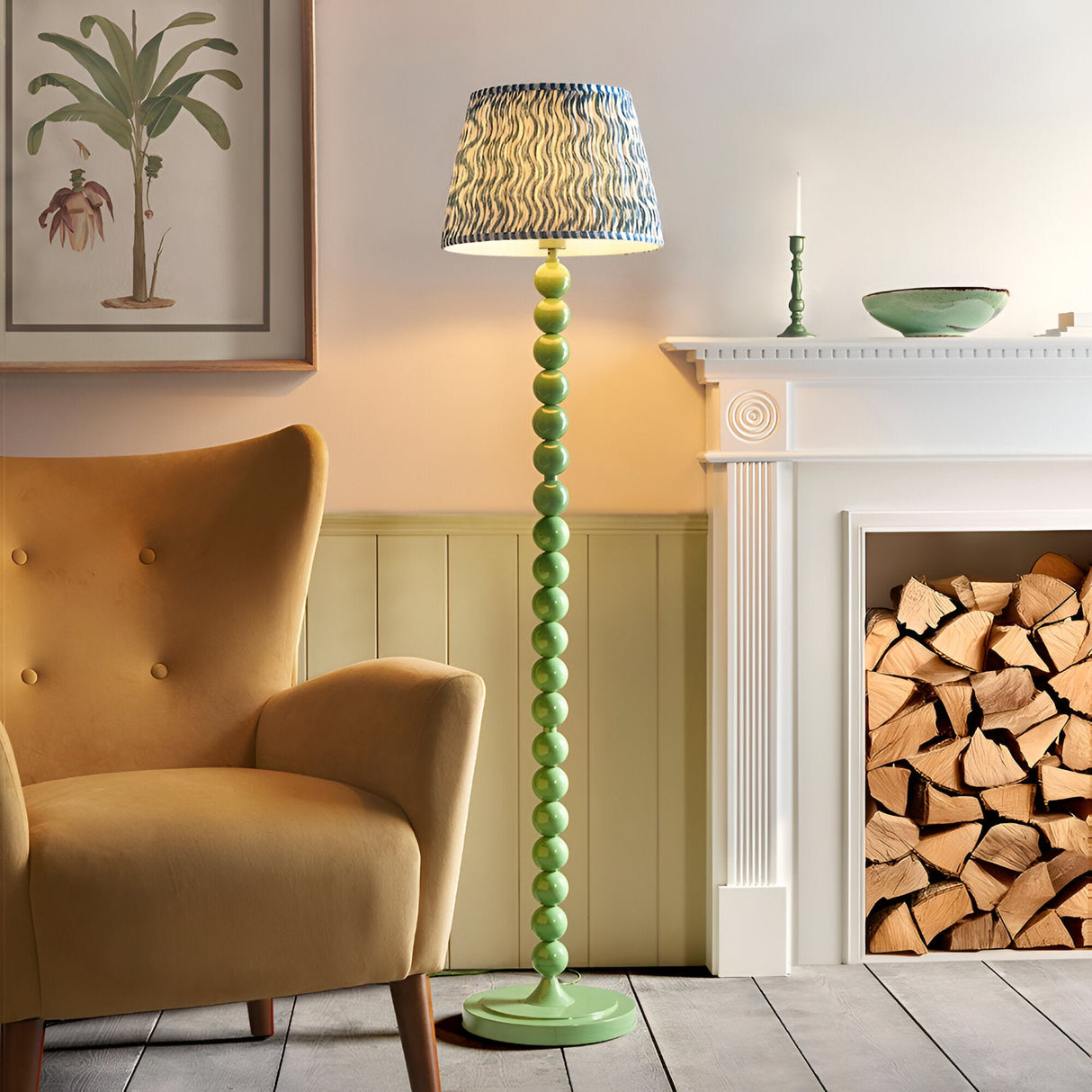 Endon Brenleigh floor lamp with green stacked sphere base and blue Ripple pleated shade, beside a mustard armchair and white fireplace with logs.